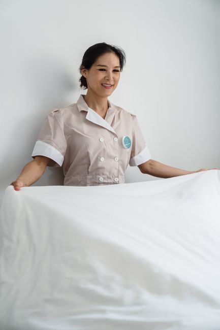 Smiling housekeeper changes bed linen in a clean, bright room. Ideal for hospitality and cleaning services imagery.